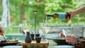 Una mesa de comedor con dos copas de vino, una botella de vino siendo servida, y una persona sosteniendo un tenedor.