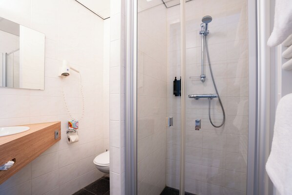 Un baño moderno con ducha envuelta en vidrio, tocador de madera, inodoro y espejo.