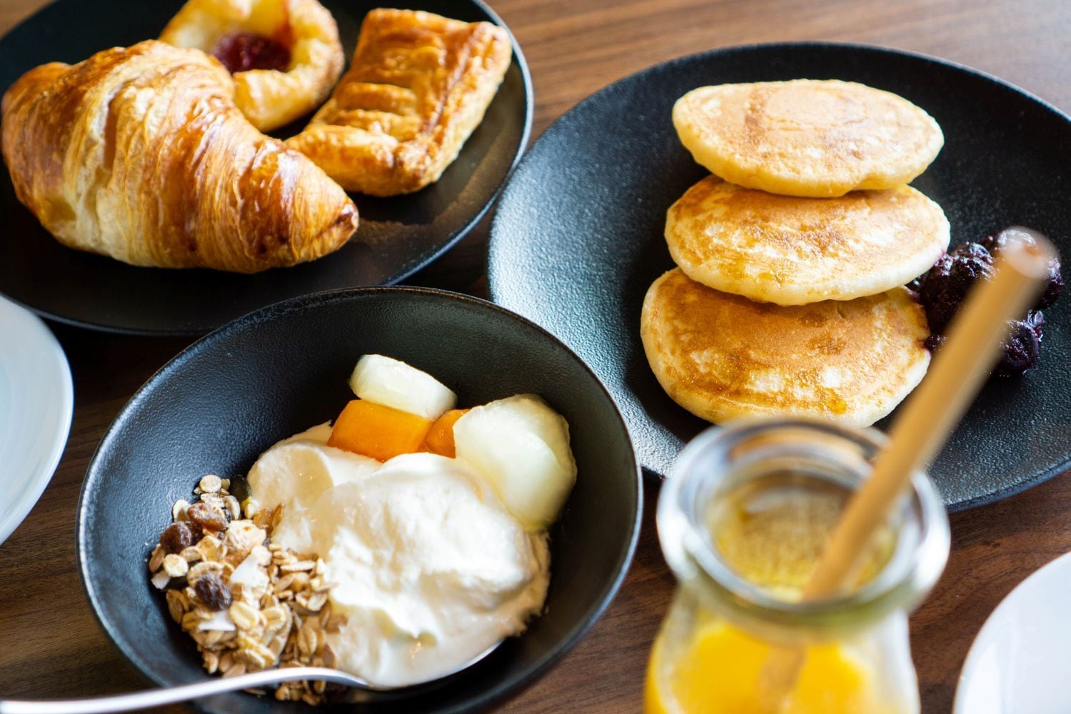 Een ontbijt met croissants, pannenkoeken, yoghurt met fruit en granola.