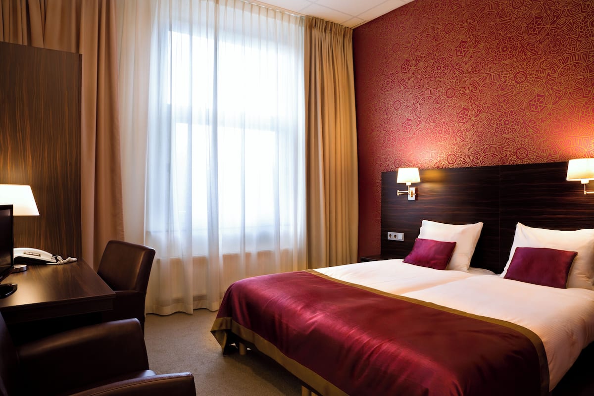 A hotel room with a large bed, two bedside lamps, a desk with a telephone, and a chair.