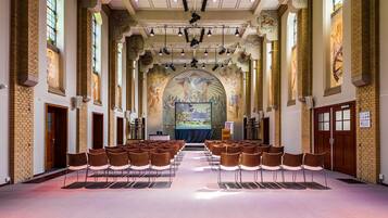 Een kerkinterieur met rijen stoelen gericht op een kansel en altaar, grote glas-in-loodramen en een muurschildering.