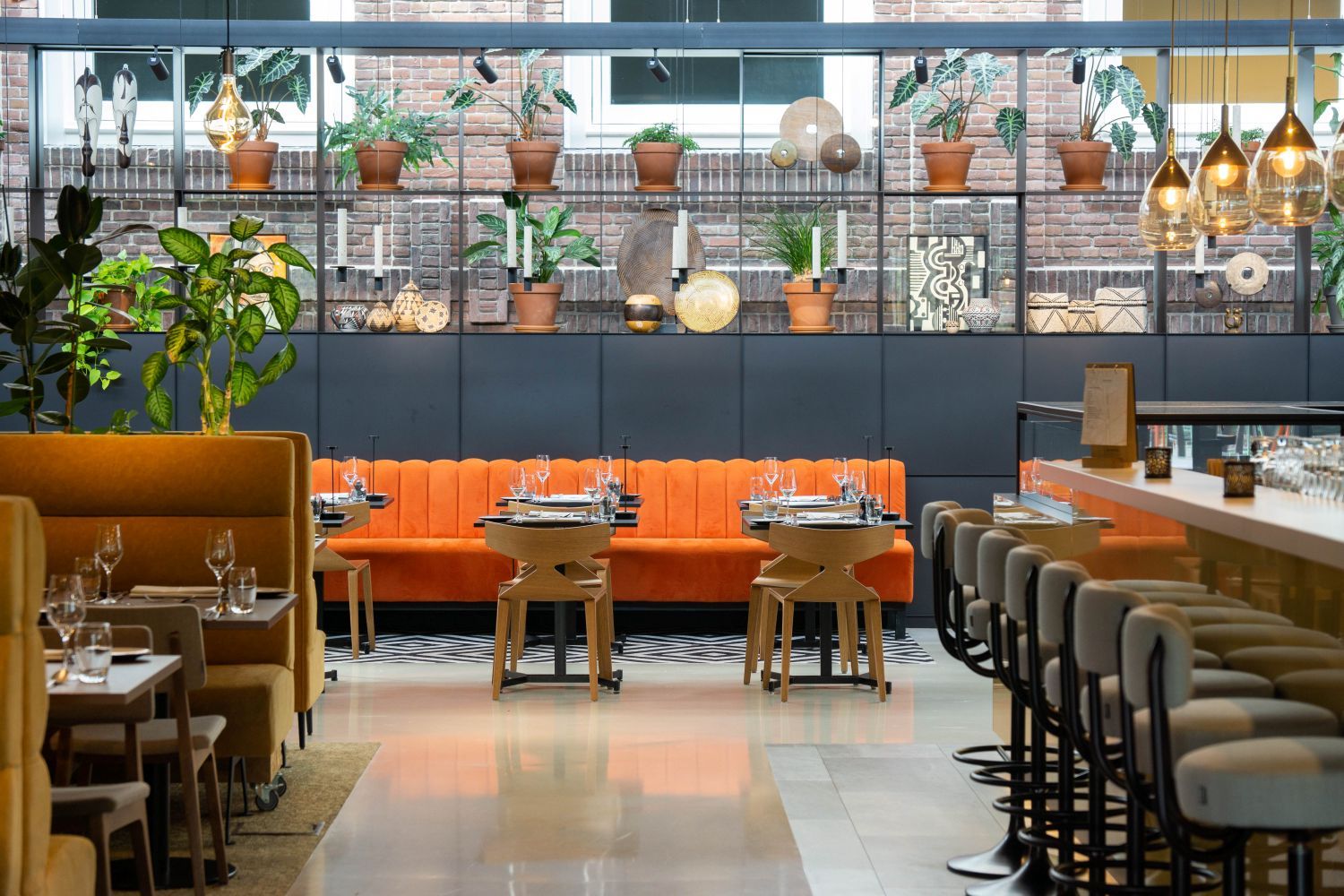L’intérieur d’un restaurant avec un mur en briques, des sièges orange, des tables en bois et des plantes suspendues.