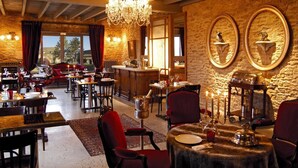 A restaurant with multiple tables, red chairs, a chandelier, and a stone wall.
