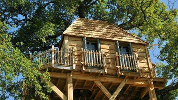 A wooden treehouse with a balcony, built on a sturdy wooden structure.