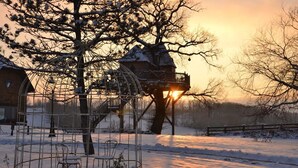 A snow-covered outdoor area with a treehouse and a brick building.