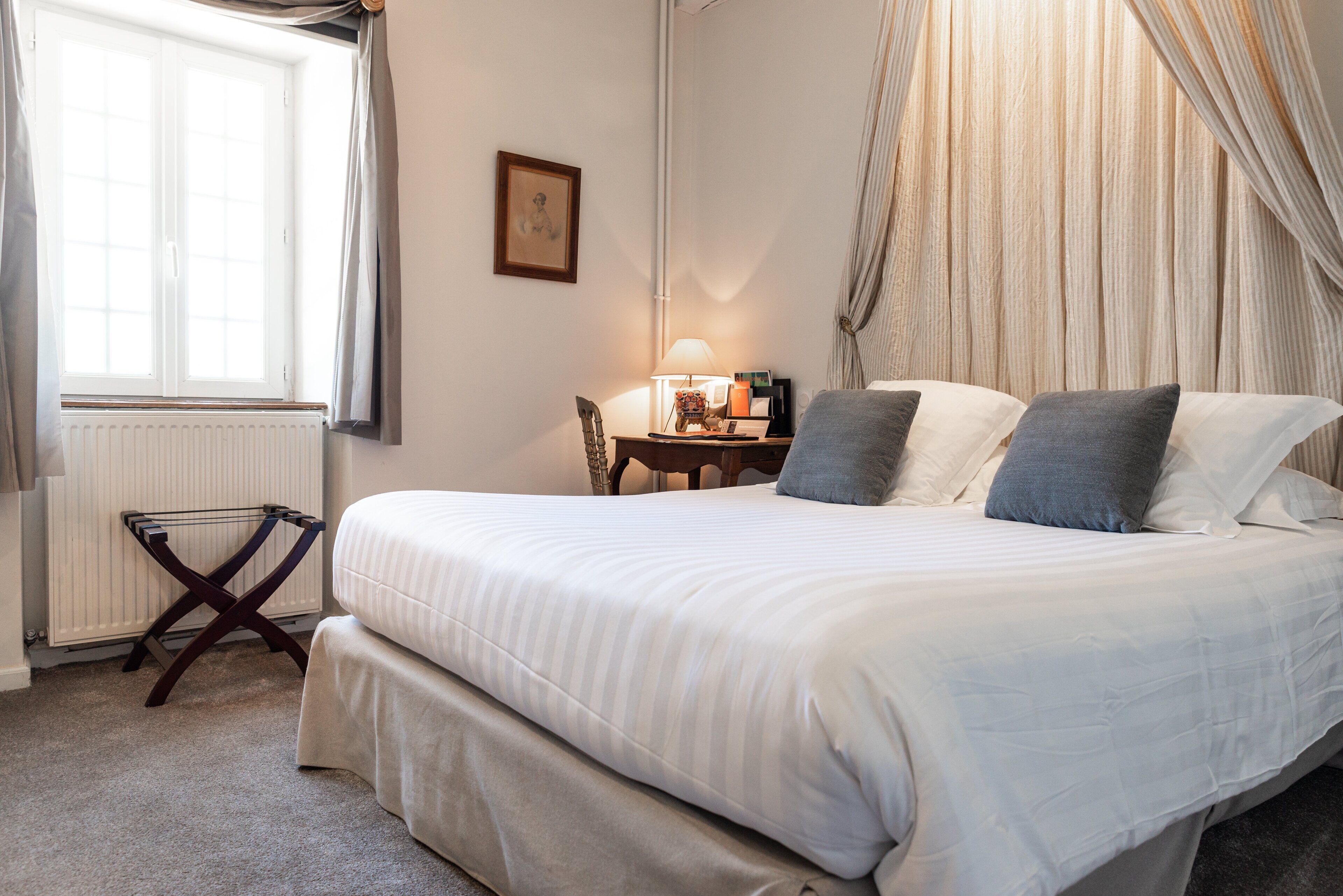 A neatly made bed with pillows, a bedside table with a lamp, a chair, and a radiator.