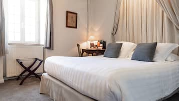 A neatly made bed with pillows, a bedside table with a lamp, a chair, and a radiator.