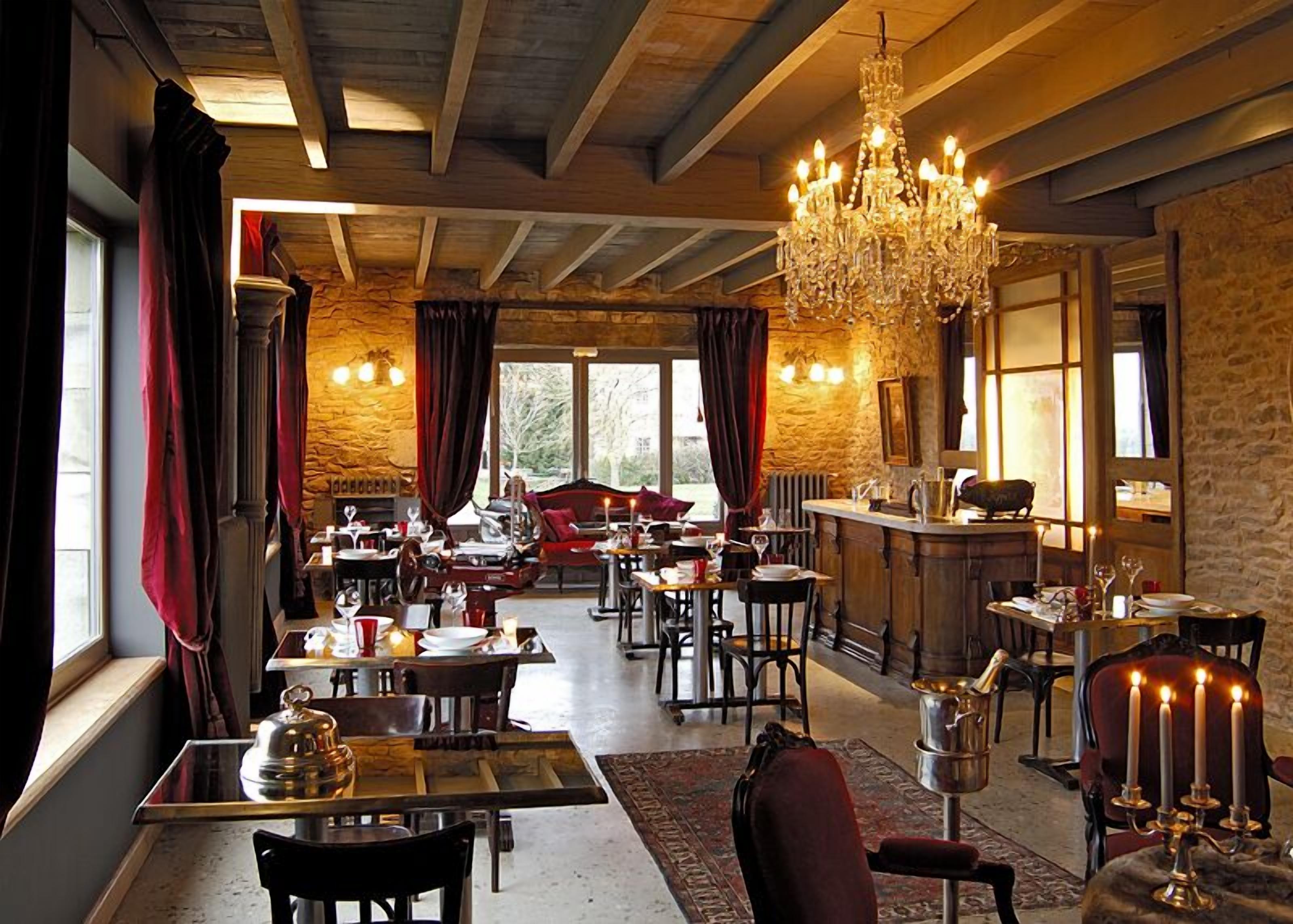 A cozy restaurant with wooden beams, a chandelier, and stone walls. Tables are set with candles and dishes.