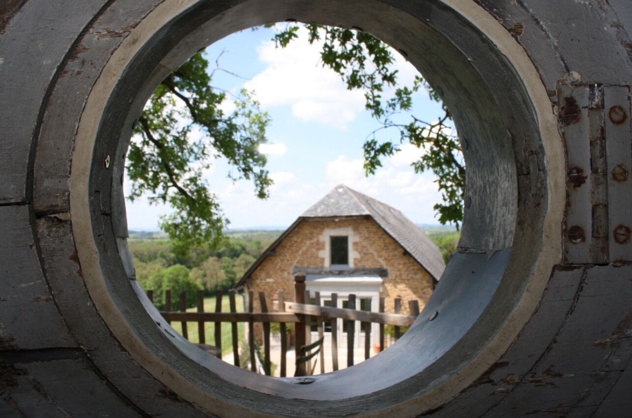 Vista a través de una ventana circular de un edificio de piedra, con una valla de madera en primer plano.