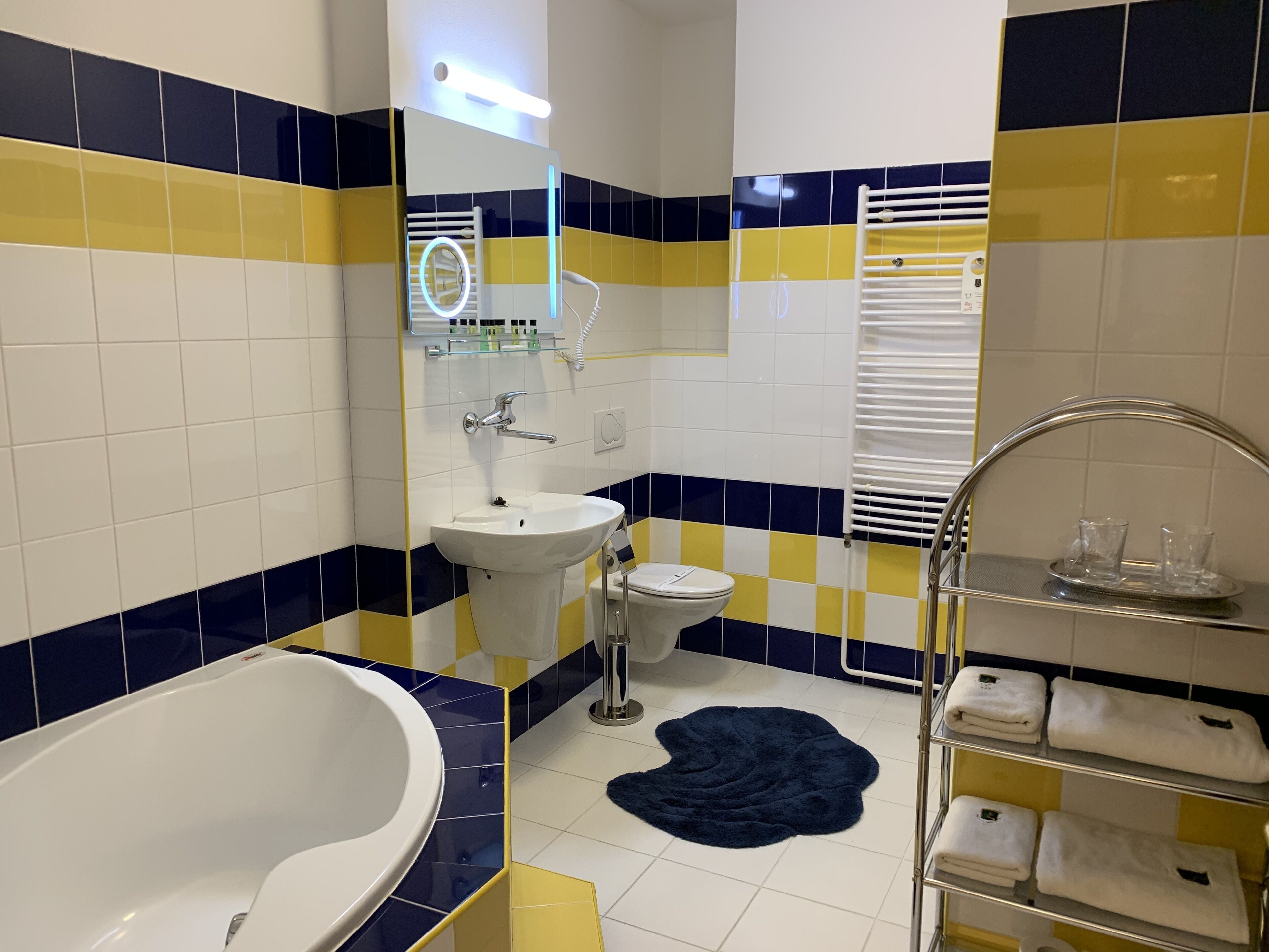 Un baño con lavamanos blanco, inodoro, bañera y toallero con toallas.