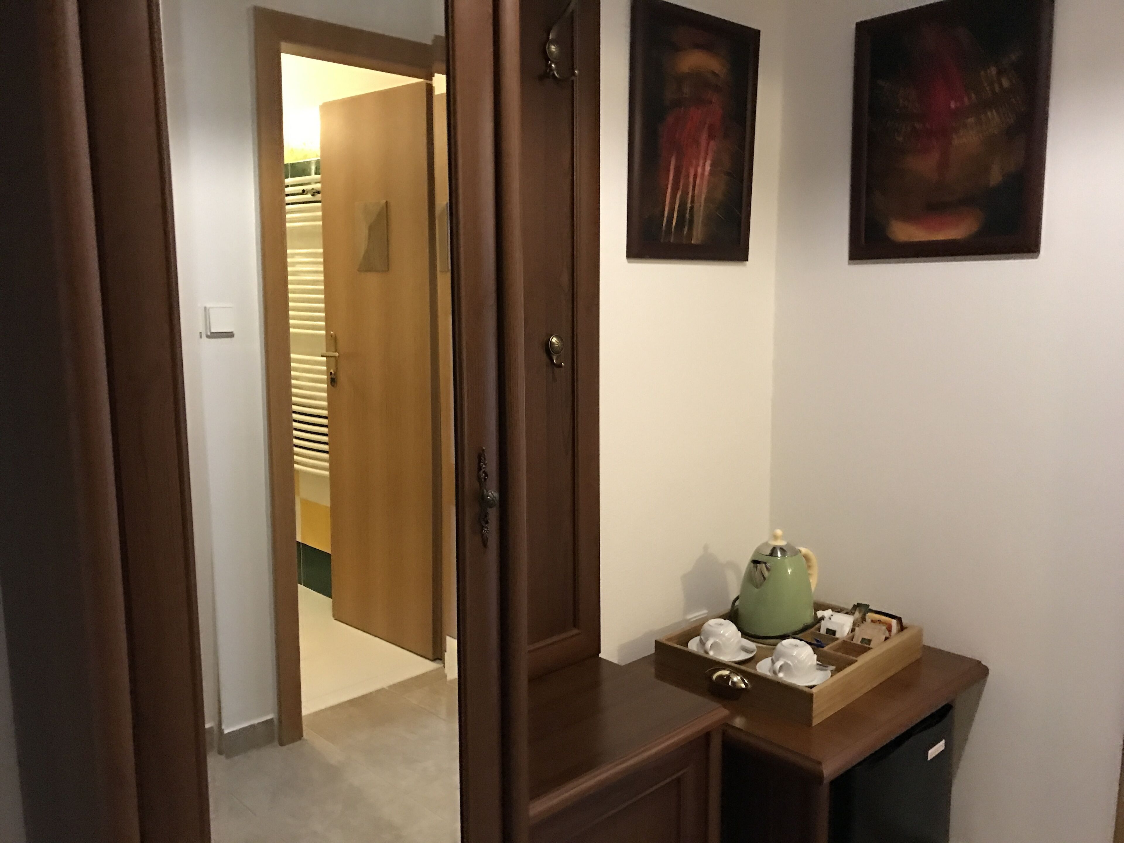 A hallway with a wooden door, a small table with a green teapot, and a wall-mounted abstract painting.
