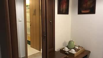 A hallway with a wooden door, a small table with a green teapot, and a wall-mounted abstract painting.