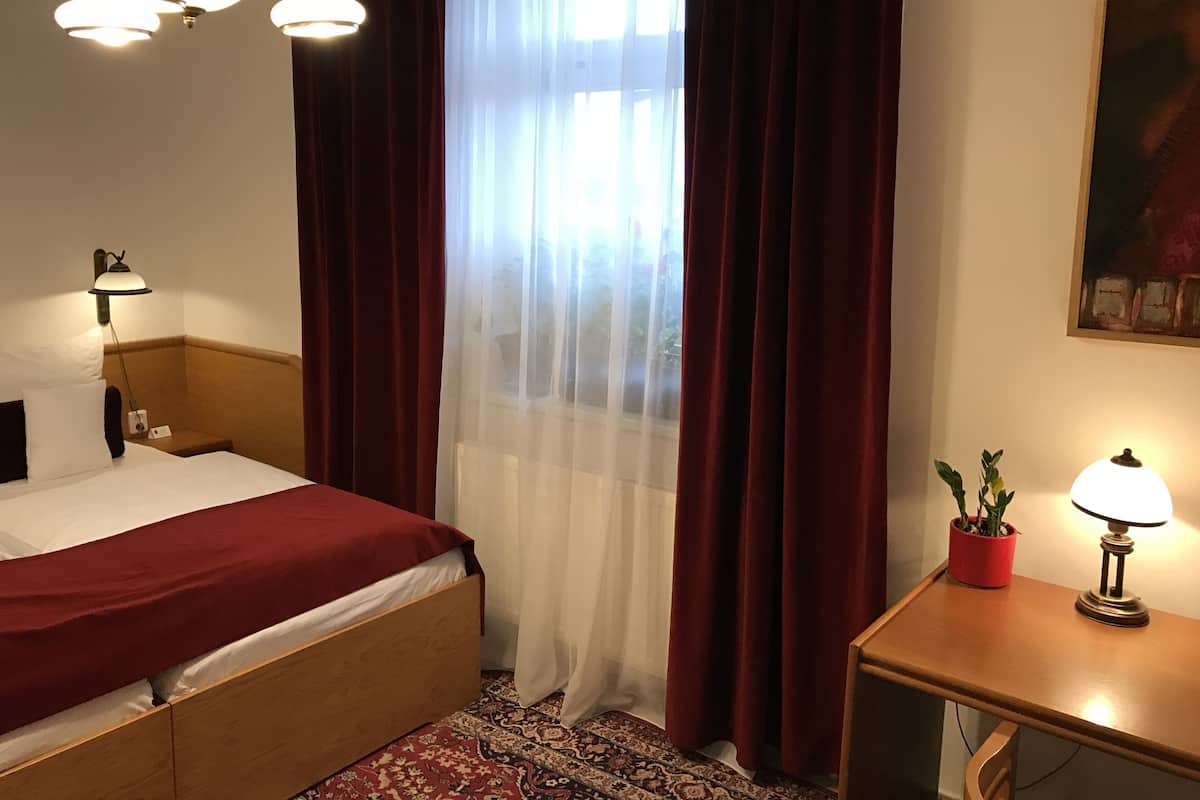 Ein Hotelzimmer mit Bett, Nachttisch mit Lampe, einer Topfpflanze und einem Bild an der Wand.