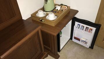 A compact kitchen area with a wooden countertop, a coffee maker, and a mini fridge stocked with beverages and snacks.