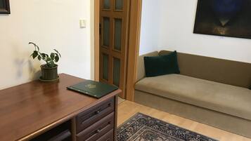 A room with a wooden desk, a potted plant, a sofa with a cushion, and a patterned rug.