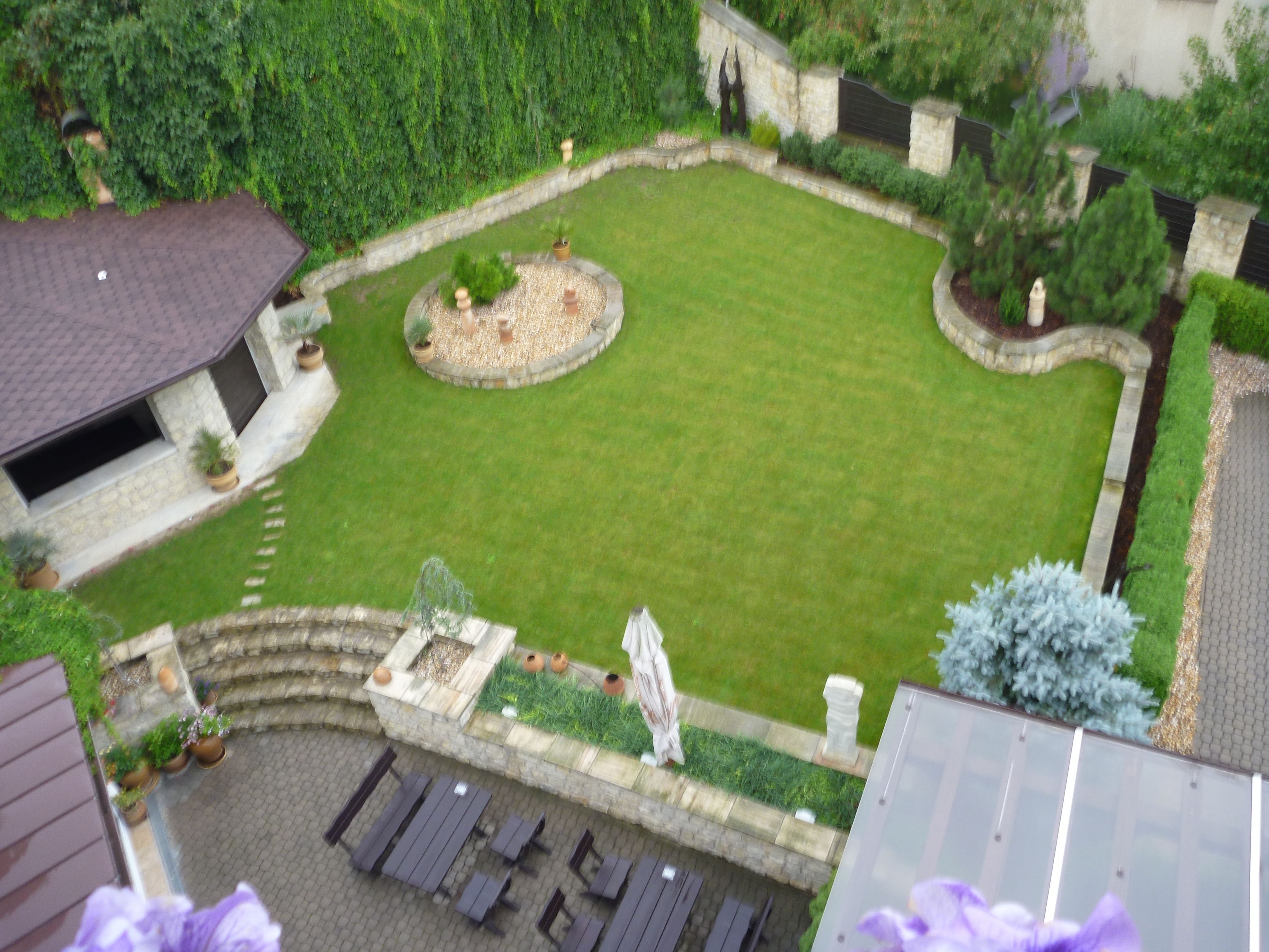 A courtyard with a lawn, stone walls, and potted plants.
