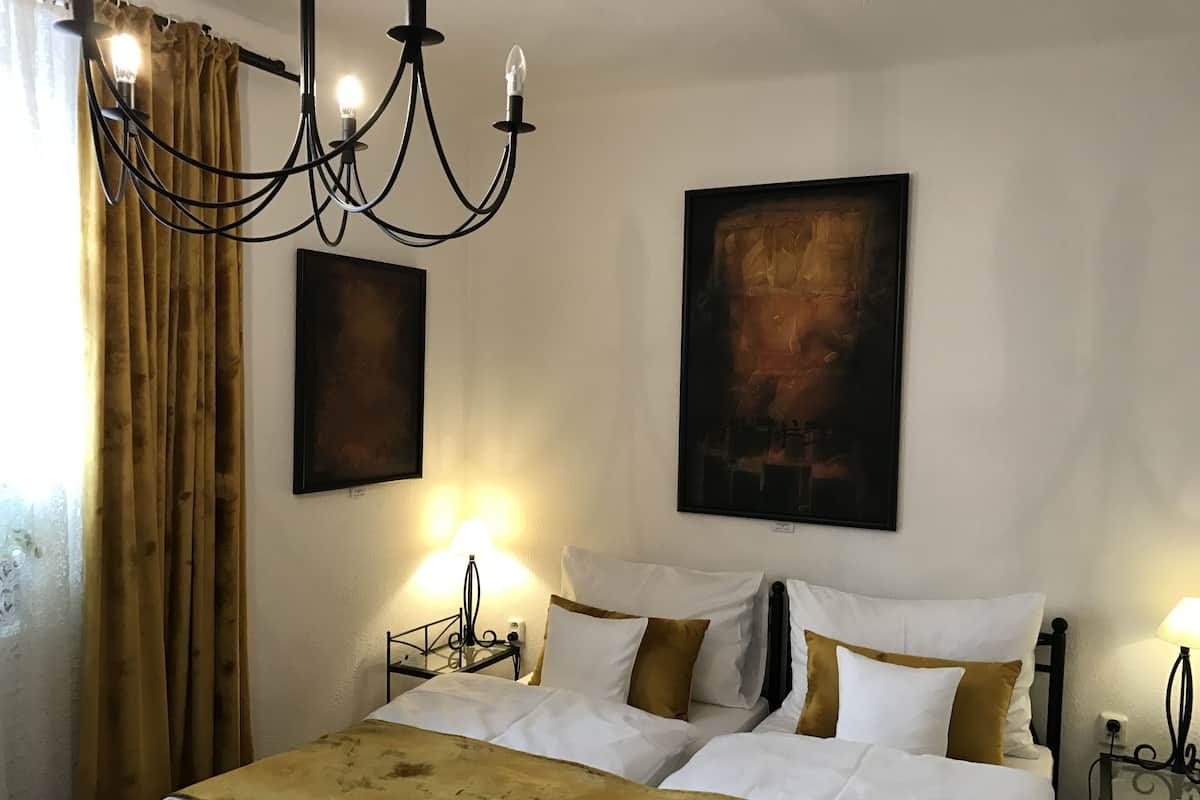 Ein Hotelzimmer mit einem großen Bett, zwei Nachttischen, einer Kronleuchter und zwei gerahmten Kunstwerken an der Wand.
