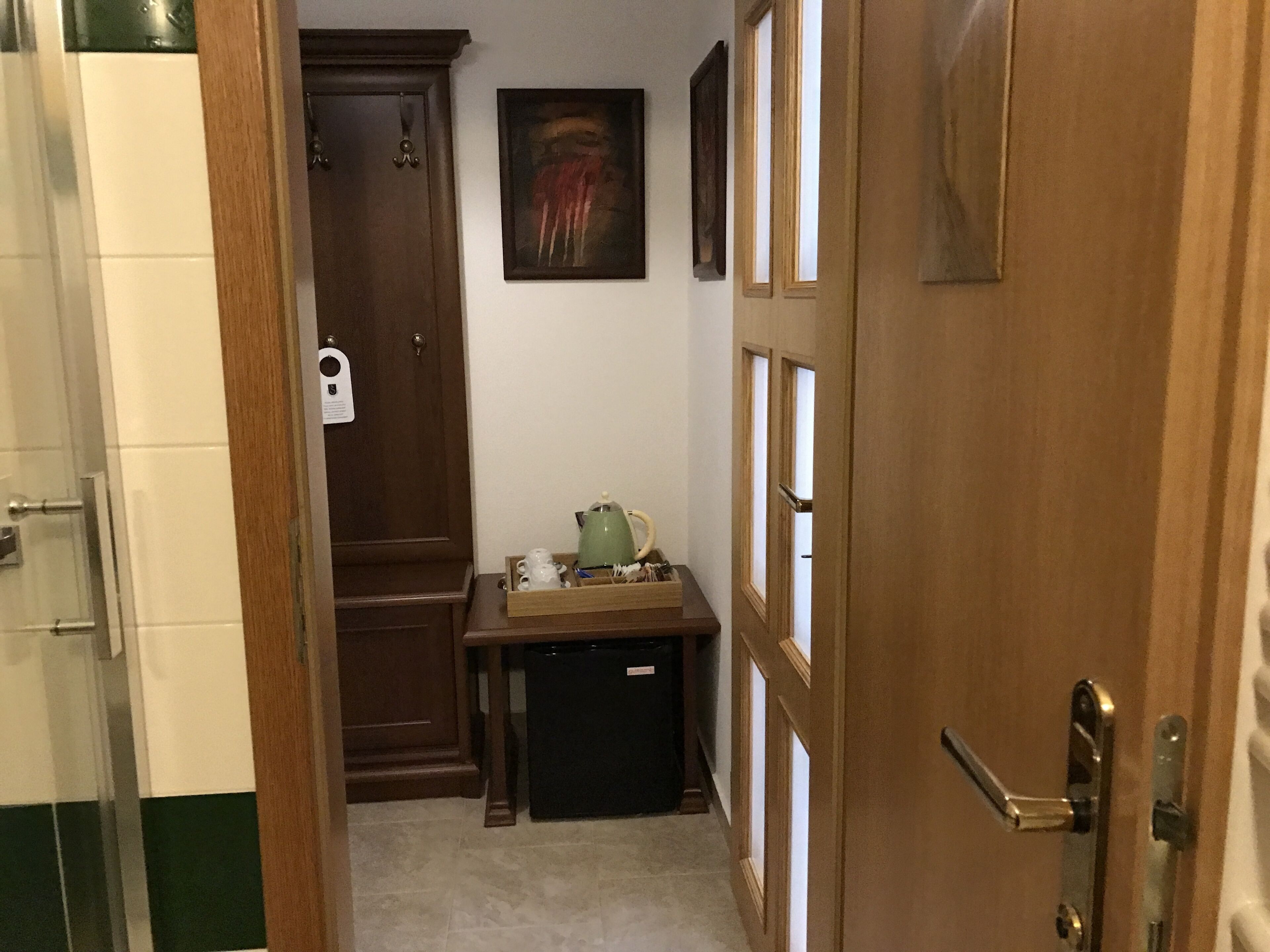 Un corridoio stretto con una porta in legno, un piccolo tavolo con un bollitore e un armadietto.