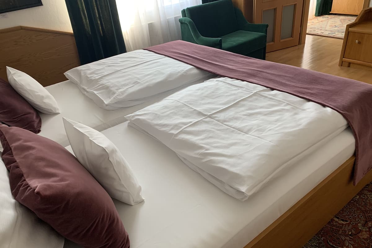 Ein Doppelbett mit weißer Bettwäsche und einer rosa Decke, ein grüner Sessel und ein Nachttisch aus Holz.