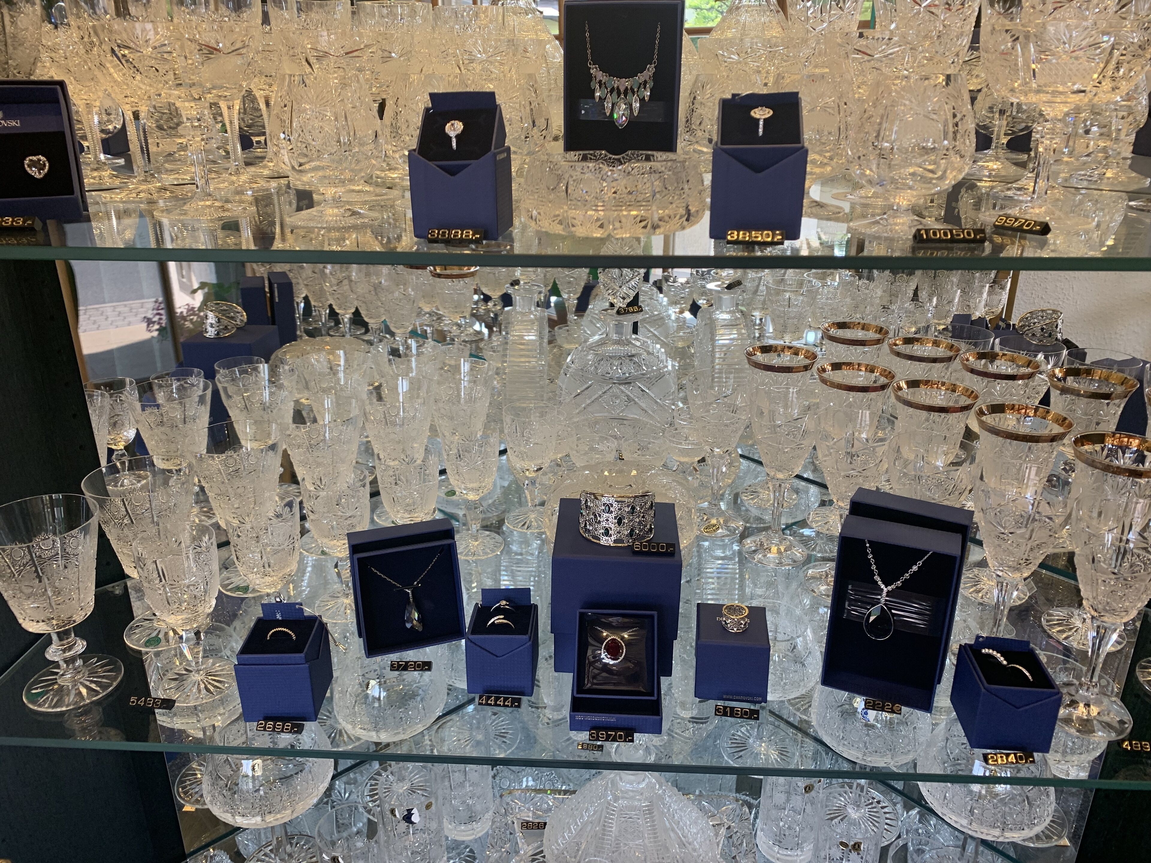 A display of various jewelry items, including rings and bracelets, each in a numbered box, set against a backdrop of numerous crystal glassware items.