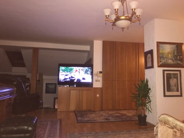 A living room with a TV on a wooden stand, a chandelier, and framed pictures on the wall.