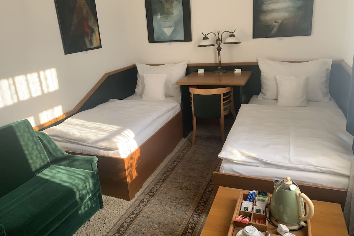 Ein Hotelzimmer mit zwei Einzelbetten, einem Schreibtisch, einem Sessel, einem grünen Sofa und einem Couchtisch mit Wasserkocher und Teebeuteln.