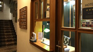 Zona de recepción de un hotel con un escritorio de madera, mostrador de recepción y una escalera que sube a un piso superior.
