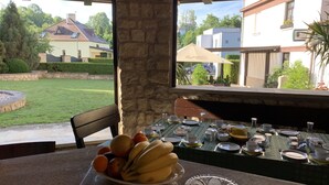 Una mesa lista para el desayuno, con frutas y vista a un jardín y edificios.