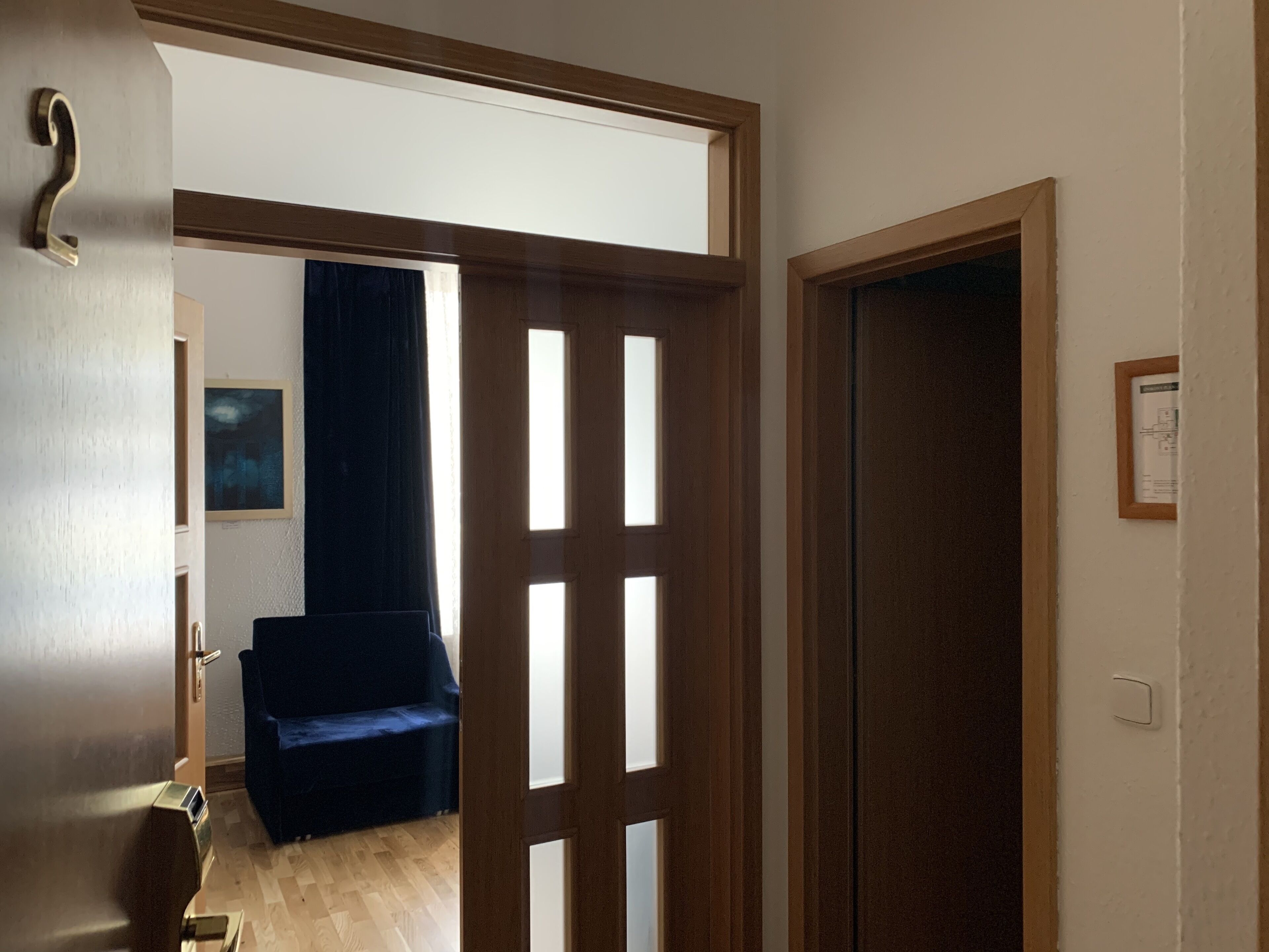 An open door leading to a room with a dark blue sofa, a framed picture on the wall, and a wooden floor.