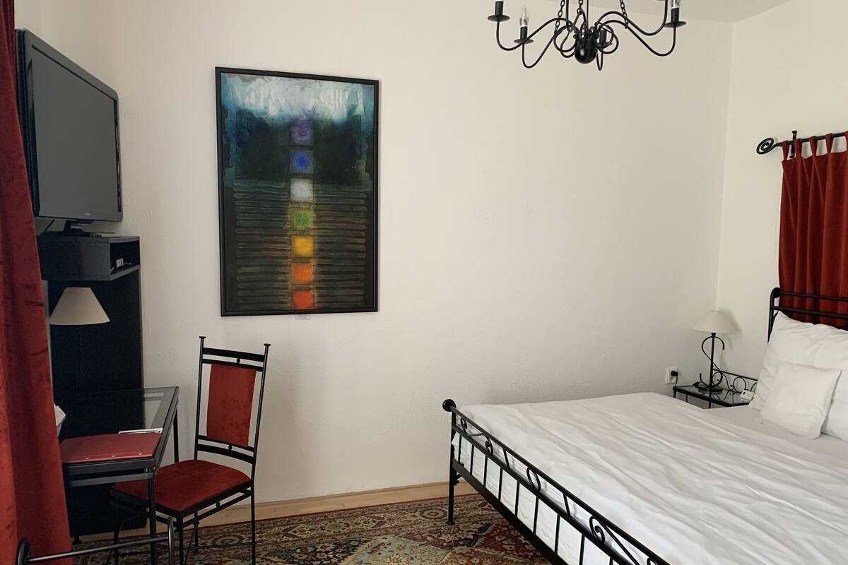 Ein Hotelzimmer mit Bett, Schreibtisch mit Stuhl, Fernseher, einer Chandelüster und einem Gemälde an der Wand.
