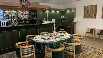 Un restaurante con zona de bar, sillas de madera, una mesa cubierta con mantel verde y una alfombra estampada.