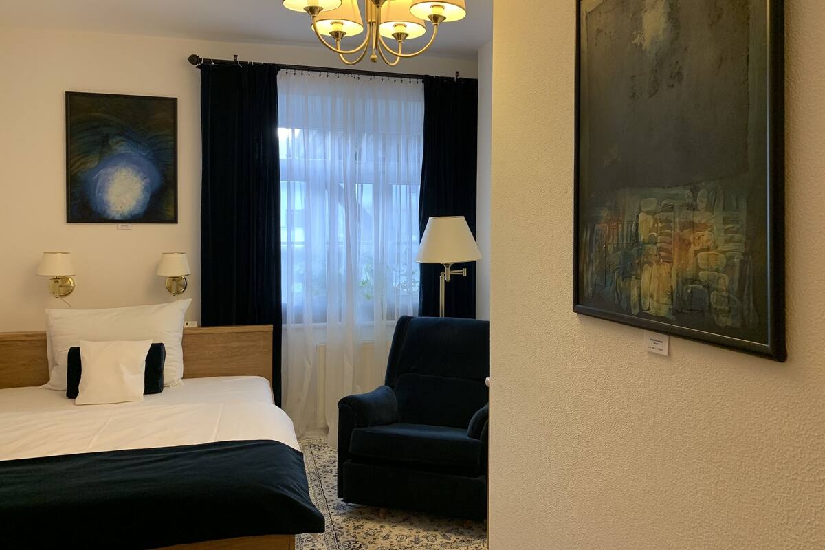 Ein Hotelzimmer mit Bett, Stuhl, Gemälde und einer Chandelier.