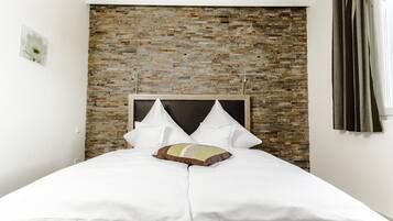 A neatly made bed with white bedding and a single decorative pillow, set against a brick-patterned wall.