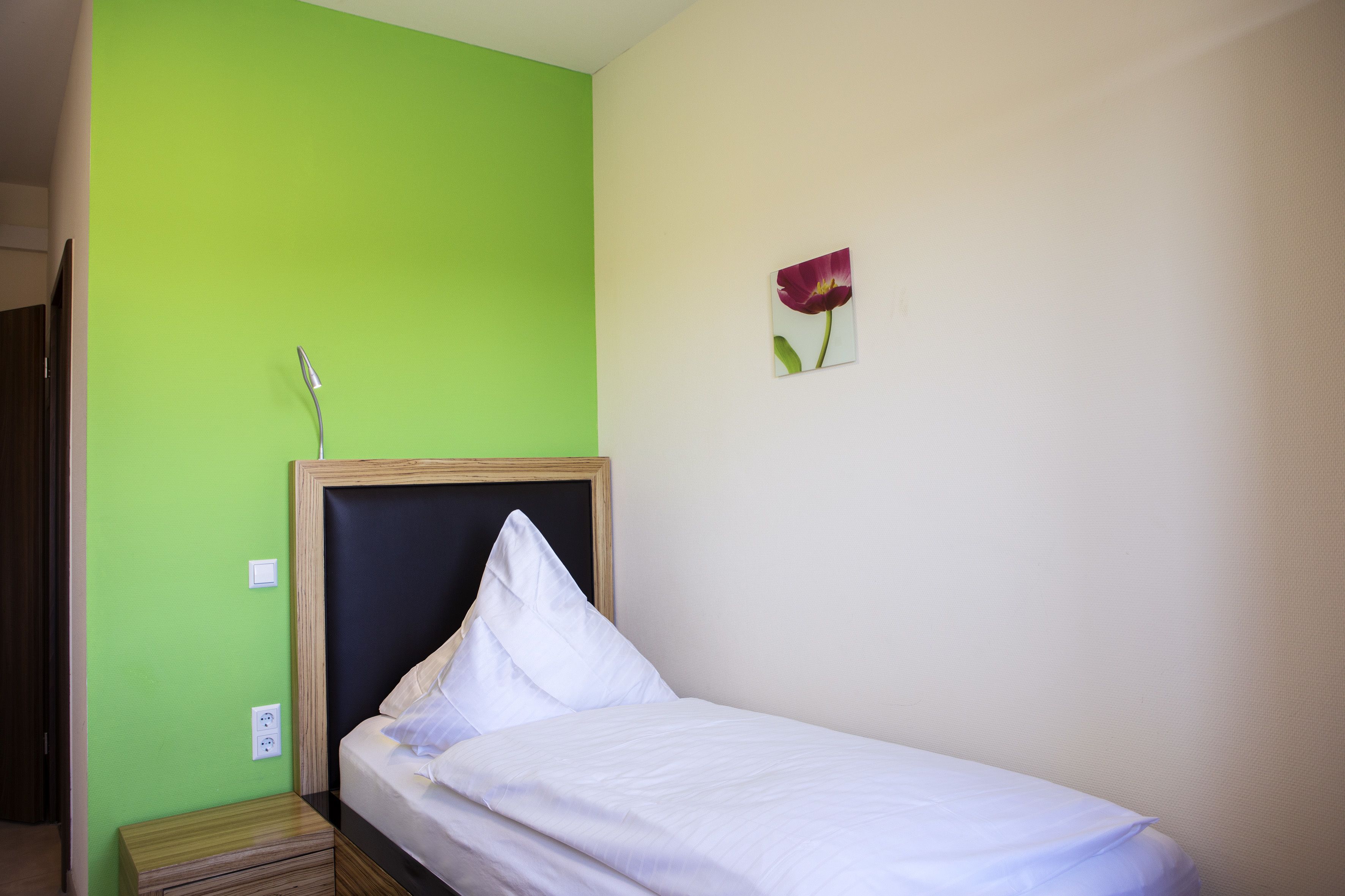 Una cama individual con cabecera de madera, una mesita de noche y una pared verde.