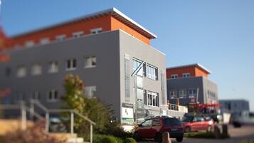 Ein modernes Gebäude mit grau-orangem Fassadenschmuck, einer sichtbaren Treppe und einem Parkplatz mit Autos.