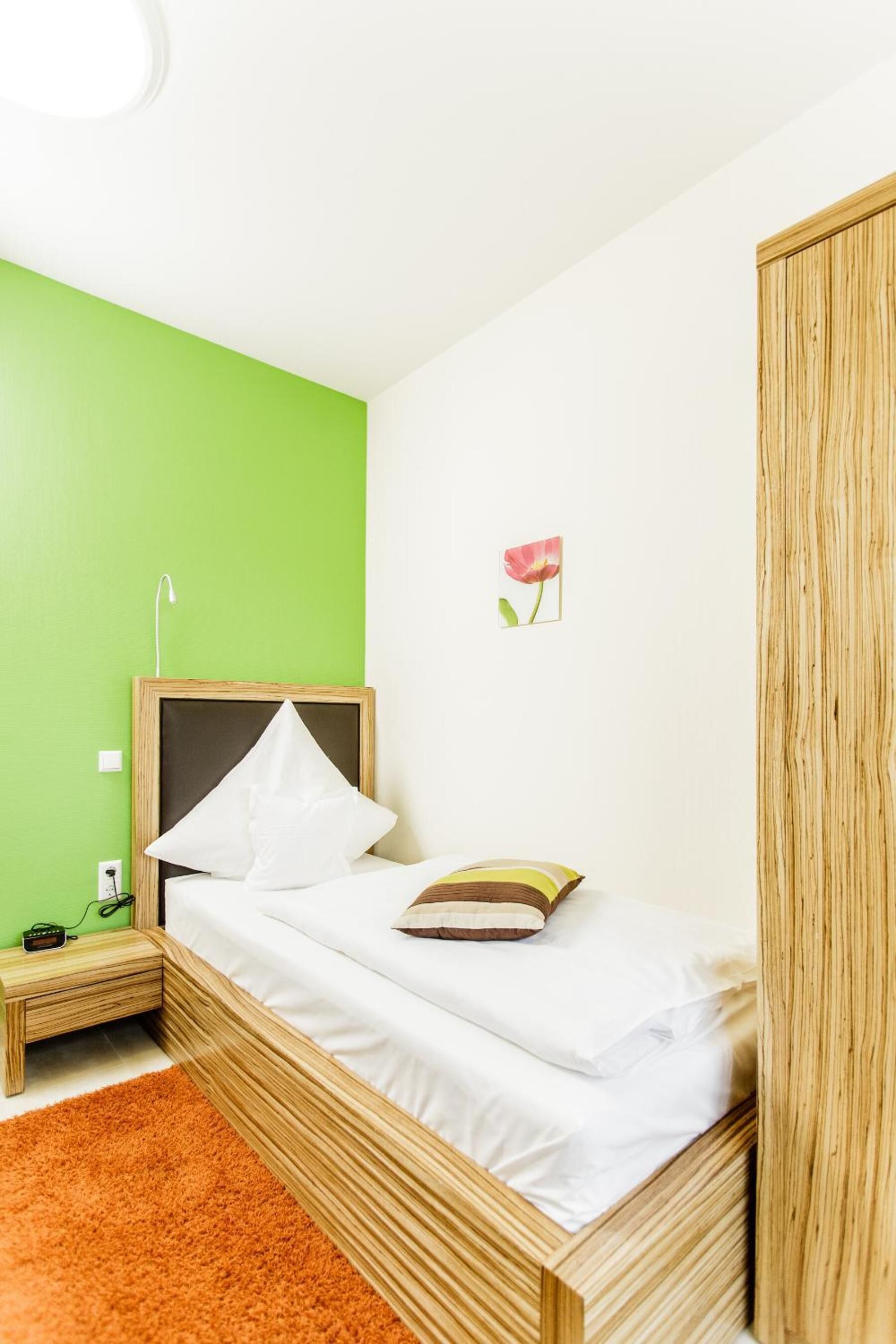 Una cama individual con estructura de madera, ropa de cama blanca y pared verde.