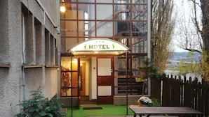 A hotel entrance with a glass facade, a green carpeted area, and wooden picnic tables. - Hotel Bohemians (Prague)