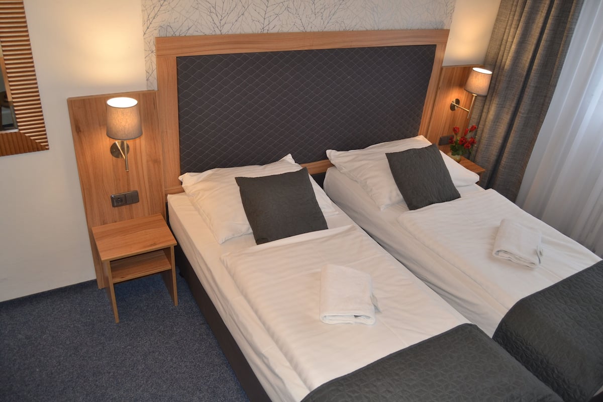A hotel room with two beds, each with a pillow, a nightstand, and a lamp.