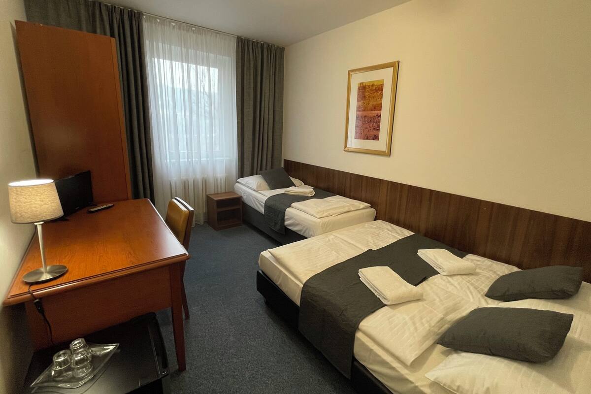 A hotel room with two beds, a desk, a chair, a lamp, and a framed picture on the wall.
