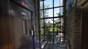 An elevator with a glass door, a small table with chairs, and a view of trees through the window. - Hotel Bohemians (Prague)