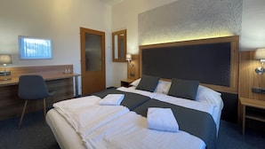A hotel room with a large bed, a desk, a chair, a mirror, and a wall-mounted lamp. - Hotel Bohemians (Prague)