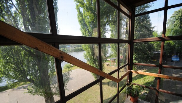 A view from a window with a wooden railing, overlooking a river, trees, and a small building. - Hotel Bohemians (Prague)