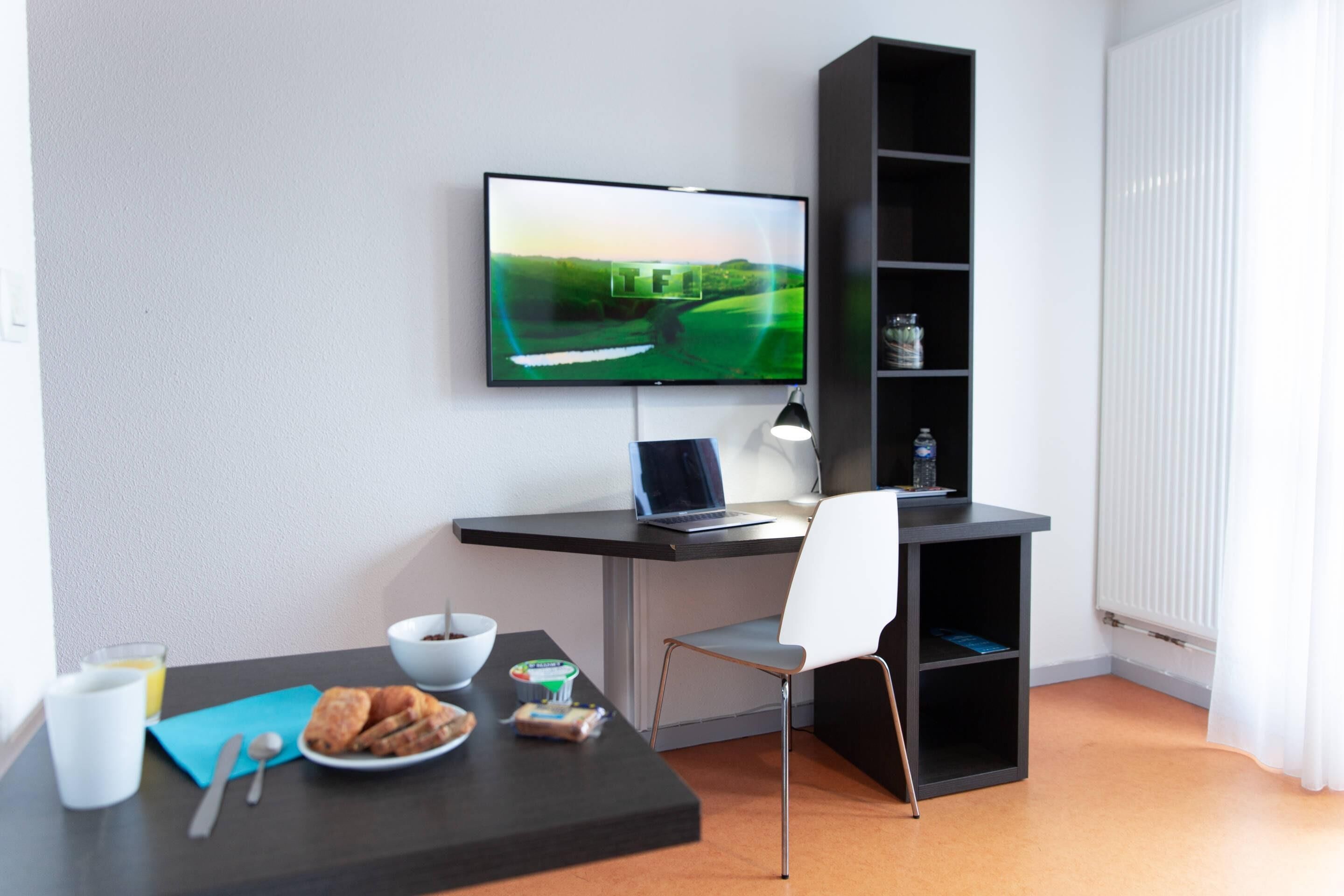 A modern room with a desk, chair, TV, and a shelf with a water bottle.