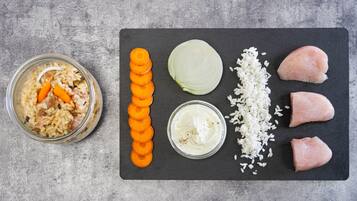 A meal prep with rice, carrots, cabbage, chicken, and a bowl of sauce on a slate board.