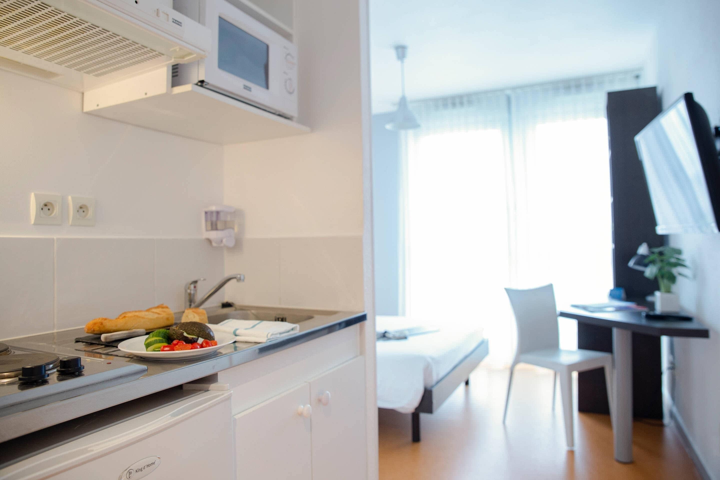Habitación de hotel pequeña con kitchenette, una cama, escritorio y una silla.