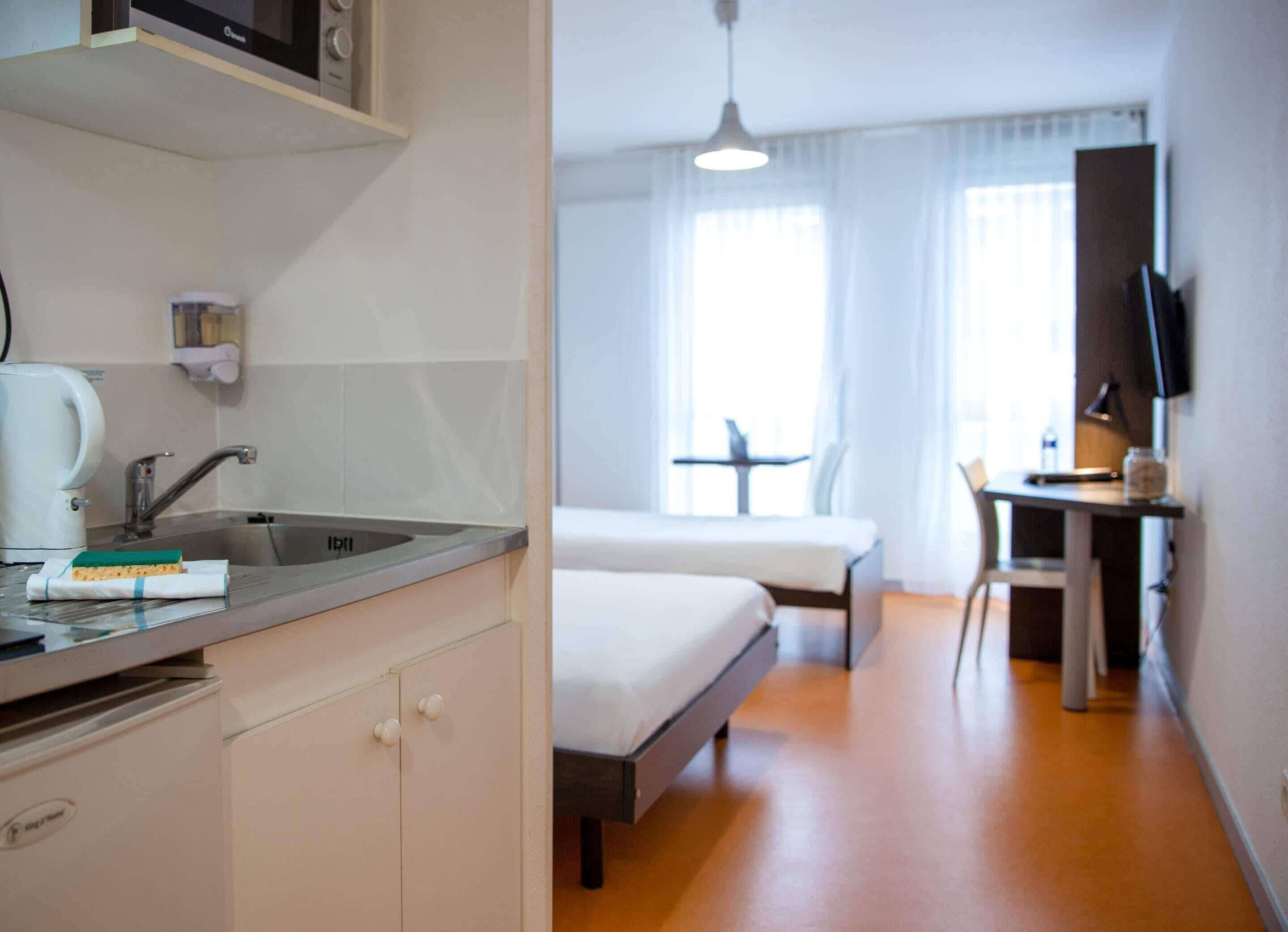 Een hotelkamer met een kitchenette, een bed, een bureau en een televisie.