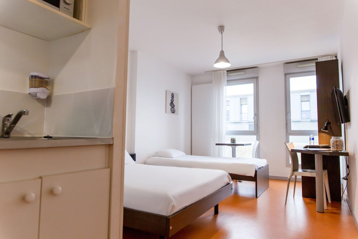 Habitación de hotel con dos camas, un escritorio, una silla, un ventanal y una lámpara en el techo.