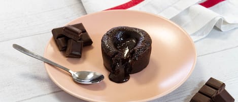 A plate with a chocolate lava cake, a spoon, and chocolate pieces on a white wooden surface.