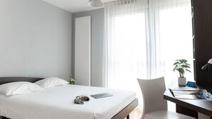 Una habitación de hotel moderna con una cama, un escritorio con una computadora portátil, una silla y una planta en maceta.