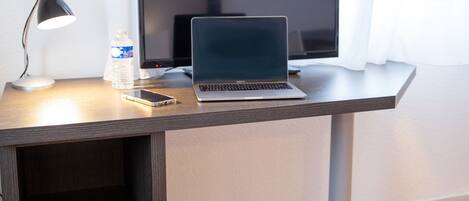 Un escritorio con una computadora portátil, un teléfono inteligente, una botella de agua y una lámpara de mesa.